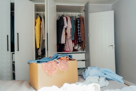 A cardboard box of selected clothes for donating to a Charity shop standing on the bed. Decluttering