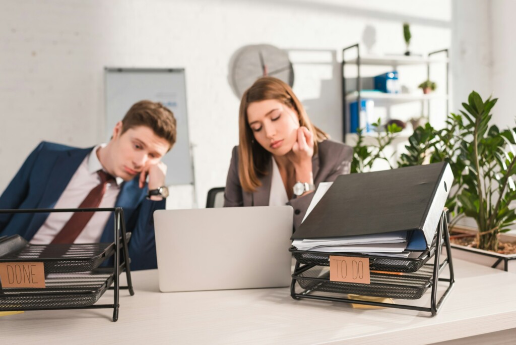 selective focus of document trays with lettering near sleepy coworkers, procrastination concept
