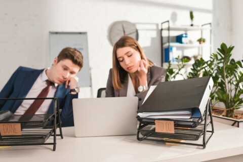 selective focus of document trays with lettering near sleepy coworkers, procrastination concept