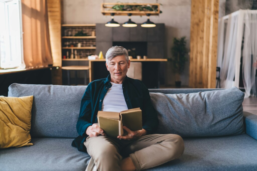Mature man reading book while sitting on comfortable sofa