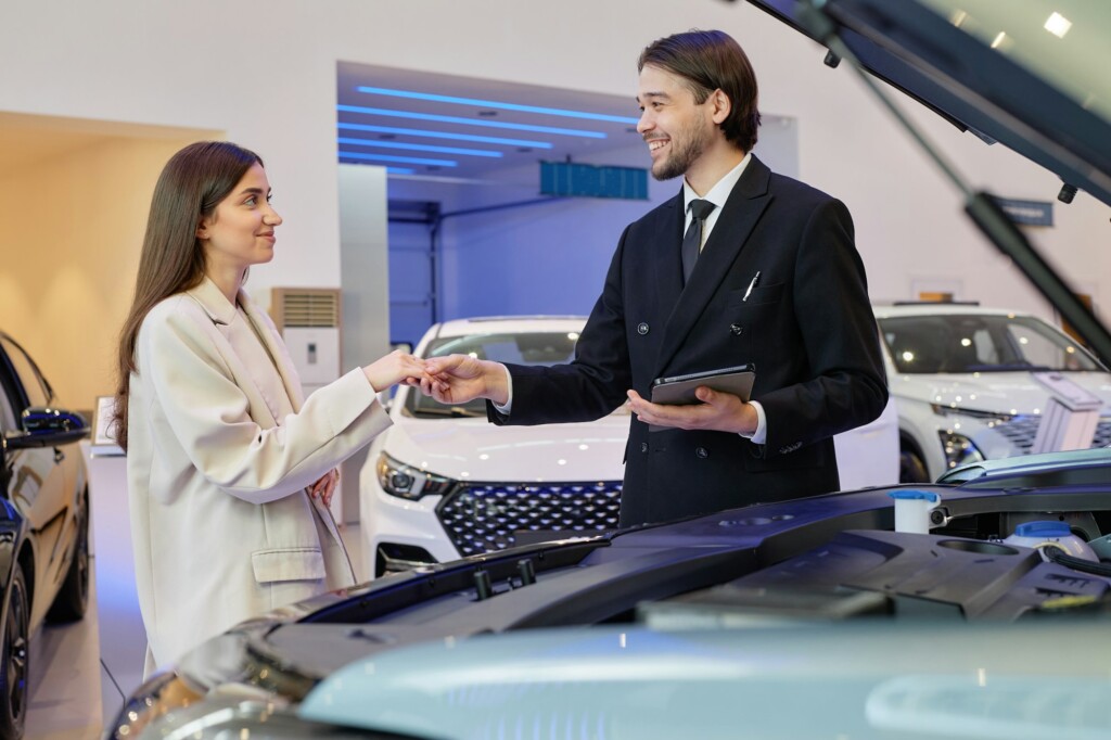 Smiling Auto Dealer Taking Customer Hand Making Deal at Dealership Center